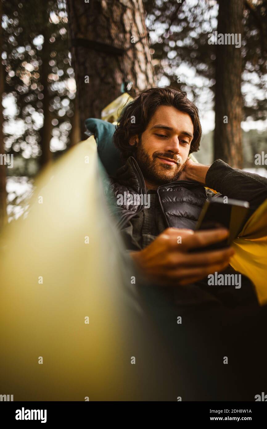 Hombre joven usando el teléfono móvil mientras estaba acostado sobre una hamaca bosque Foto de stock