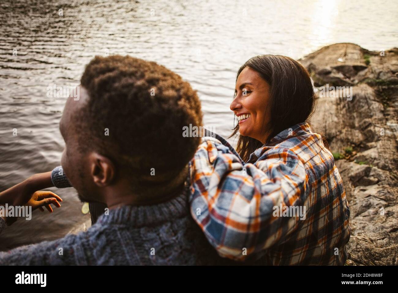 Vista lateral de una mujer sonriente y un hombre sentado junto al lago en el bosque Foto de stock