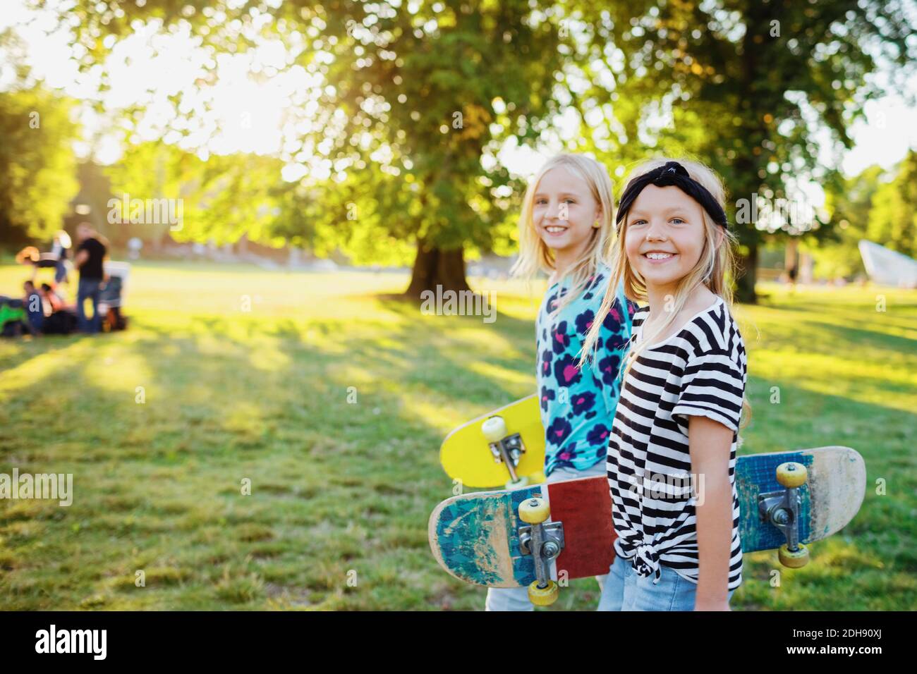 Retrato de amigos sonrientes con monopatines en el parque público Foto de stock