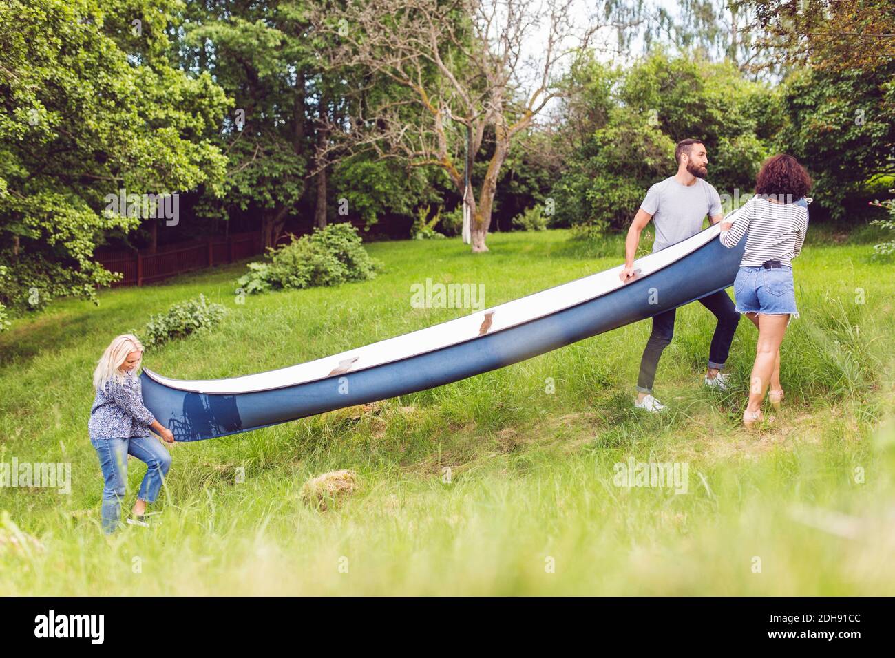 Amigos llevando canoa en el campo de hierba por los árboles Foto de stock