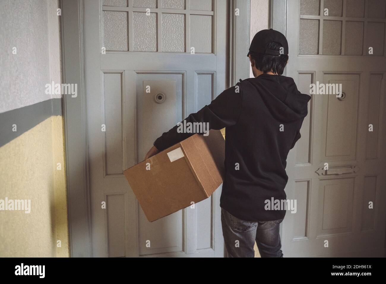 Vista trasera del hombre de la entrega con el paquete parado en la puerta Foto de stock