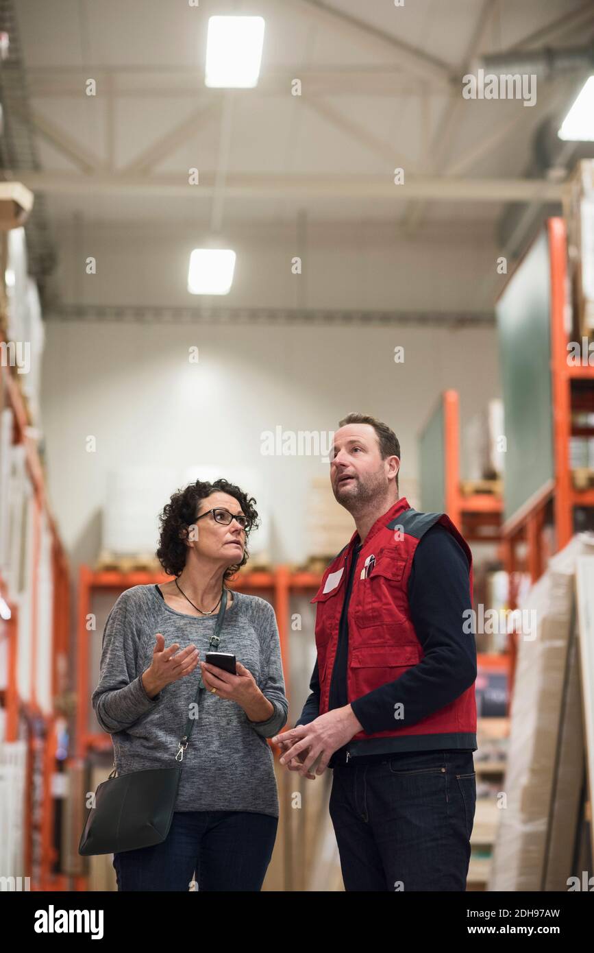 Una cliente que sostiene el teléfono inteligente mientras habla con un vendedor almacén de hardware Foto de stock