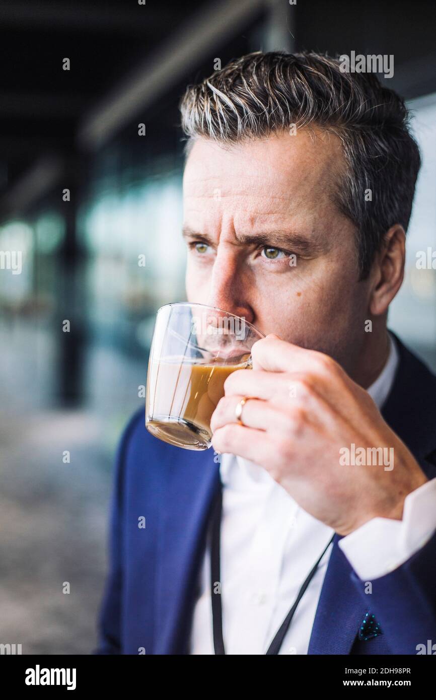 Hombre de negocios bebiendo té mientras mira fuera del lugar de trabajo Foto de stock