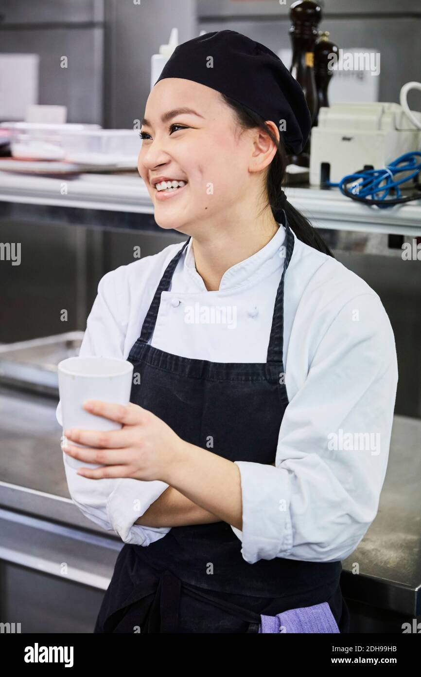Chef sonriente sosteniendo una taza desechable en la cocina comercial Foto de stock