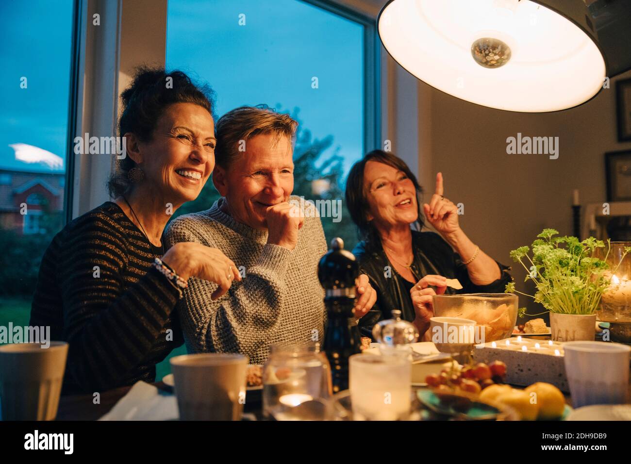 Feliz mujer mayor y hombre sentado en una mesa de comedor iluminada mientras disfruta de la cena Foto de stock