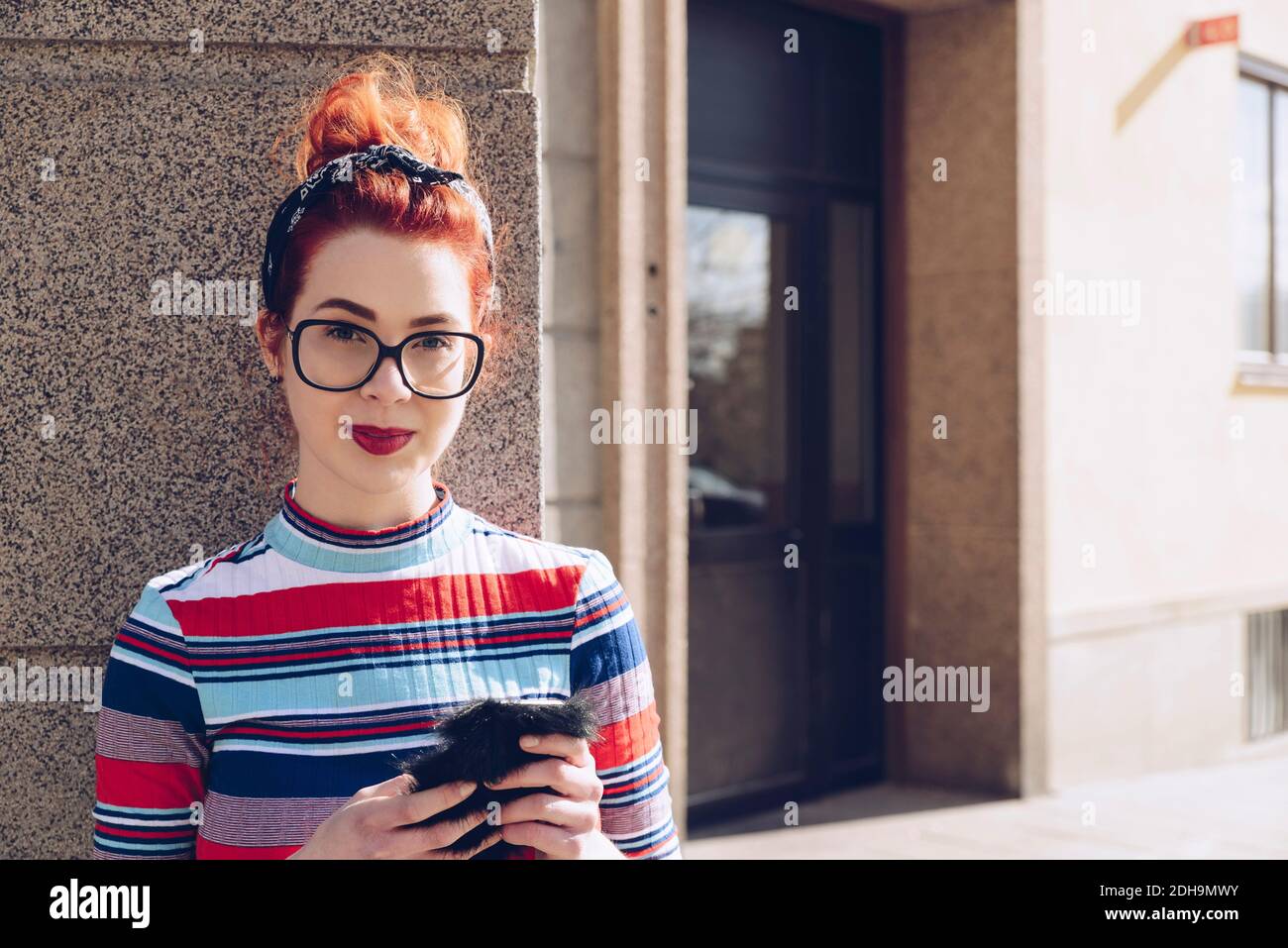 Retrato de una joven mujer hipster sosteniendo el teléfono móvil mientras estaba de pie contra la pared Foto de stock