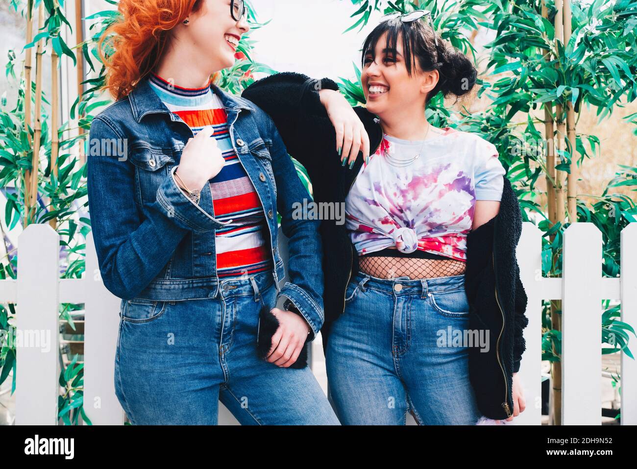 Sonriendo hipster amigas de pie contra valla Foto de stock
