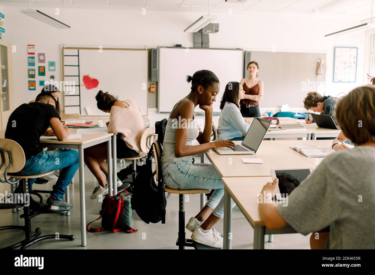 Estudiantes de secundaria estudiando mientras la maestra de pie en el aula Foto de stock