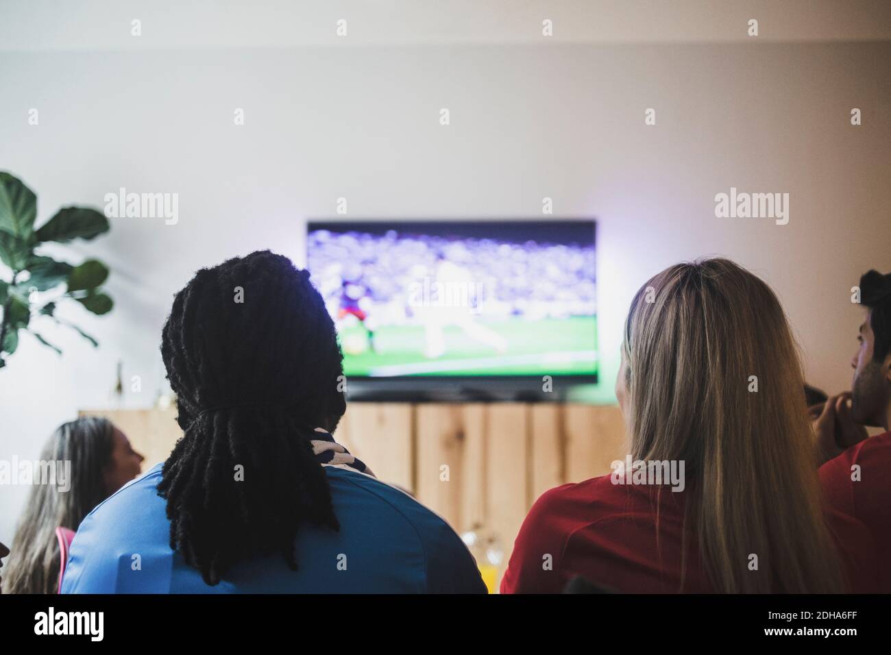 Vista trasera de amigos viendo partidos de fútbol mientras se sentaba sala de estar Foto de stock