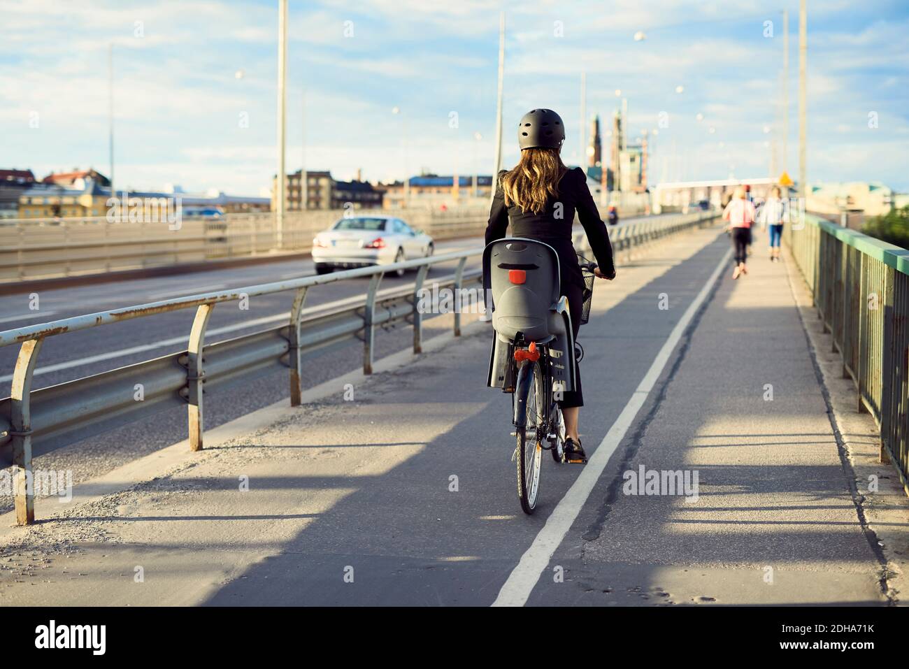 Vista trasera de la mujer de negocios en bicicleta sobre el puente contra el cielo Foto de stock