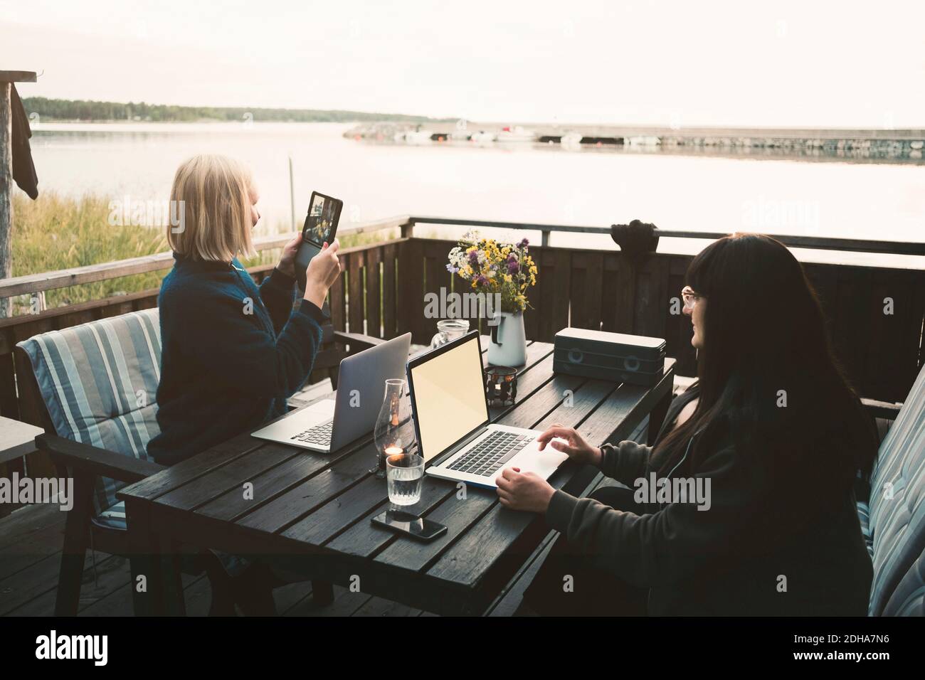 Mujer usando una tableta digital mientras se sienta con amigos sosteniendo el portátil en la mesa en la villa de vacaciones Foto de stock