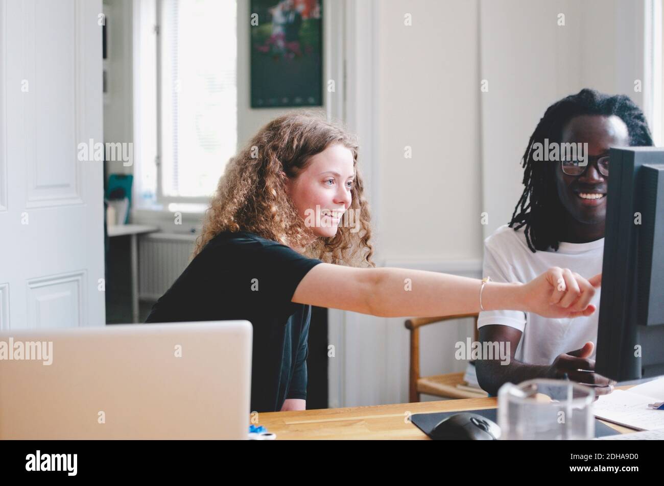 Sonriente joven empresaria mostrando algo a un colega en la computadora oficina creativa Foto de stock