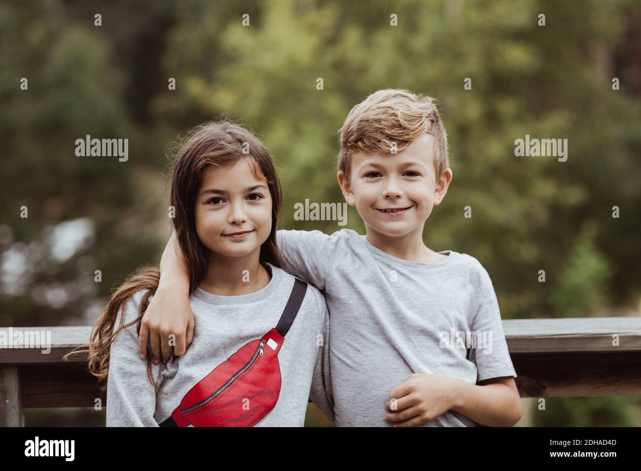 Retrato de un brazo hermano sonriente alrededor de pie con la hermana contra barandilla Foto de stock