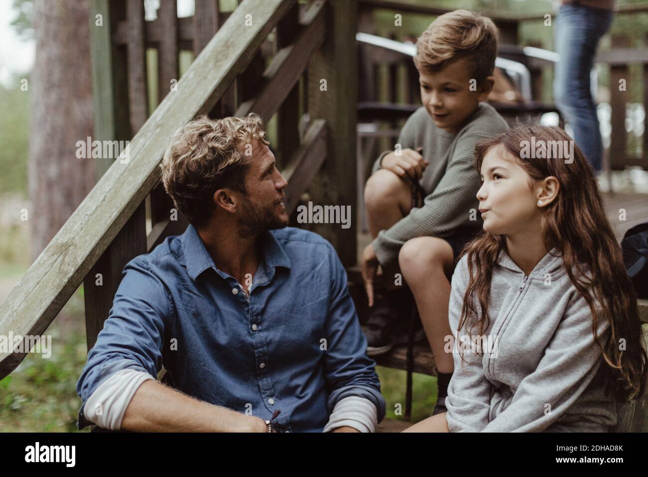 El padre y los niños pasan tiempo libre mientras están sentados en los escalones durante las vacaciones Foto de stock