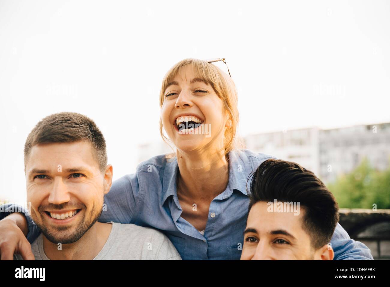 Mujer adulta media riendo mientras que de pie por amigos masculinos en reunión social Foto de stock