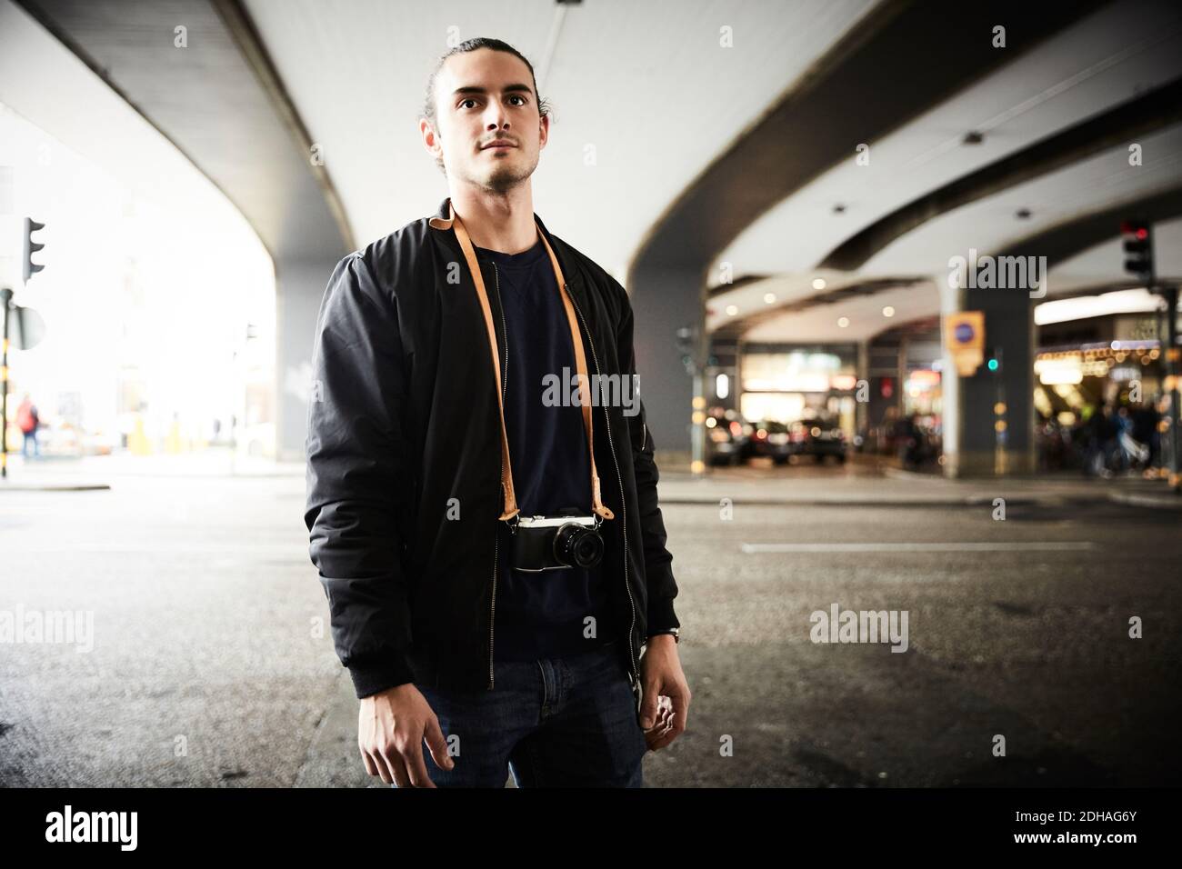Un joven con cámara de pie en la calle debajo del paso elevado ciudad Foto de stock