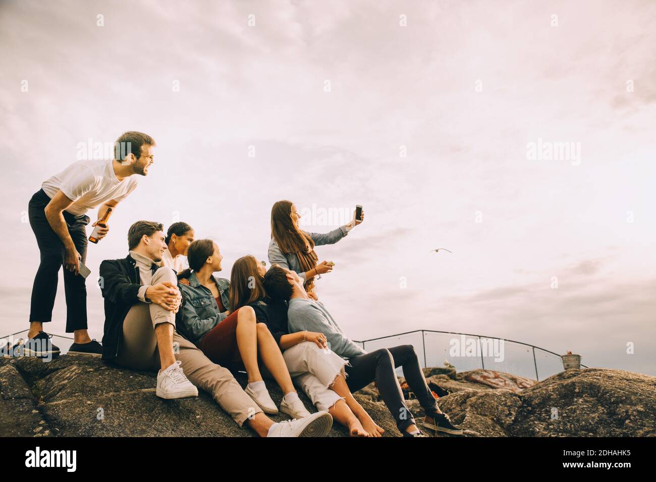 Mujer tomando selfie con amigos en formación de roca contra el cielo en picnic Foto de stock