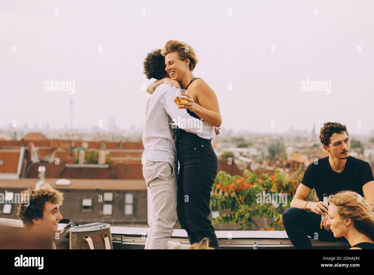 El hombre y la mujer abrazan mientras disfrutan de la fiesta con los amigos en terraza Foto de stock
