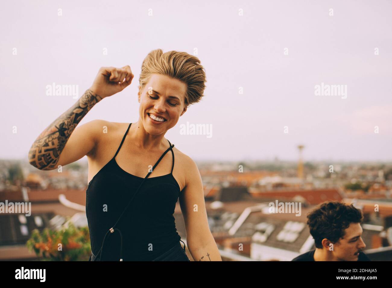 Emocionada mujer bailando mientras disfruta con un amigo en la terraza contra cielo Foto de stock