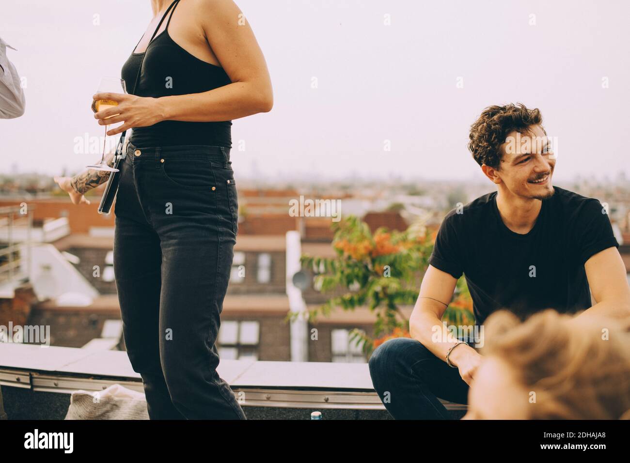 Mujer con cerveza de pie por amigo mirando en la terraza en la fiesta Foto de stock