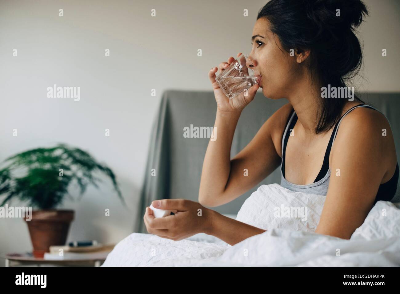 Mujer tomando medicina mientras se sienta en la cama en casa Foto de stock