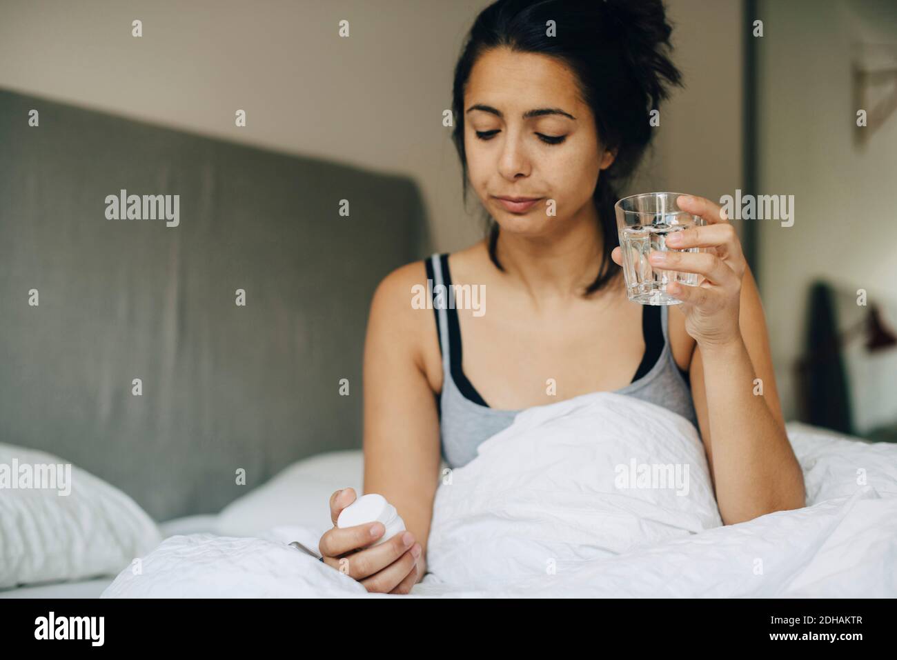Mujer mirando las píldoras mientras sostiene el vaso en la cama Foto de stock
