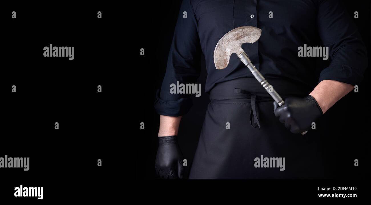 Hombre con ropa negra, guantes de látex sostiene un cuchillo de hacha de metal vintage para carne y verduras Foto de stock