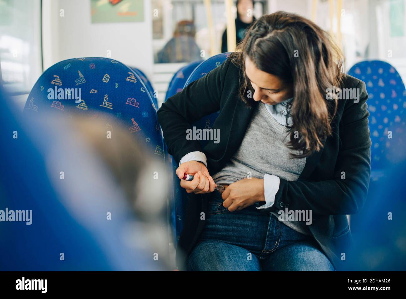 Mujer inyectándose en el abdomen mientras se sienta junto a la ventana en el tren Foto de stock