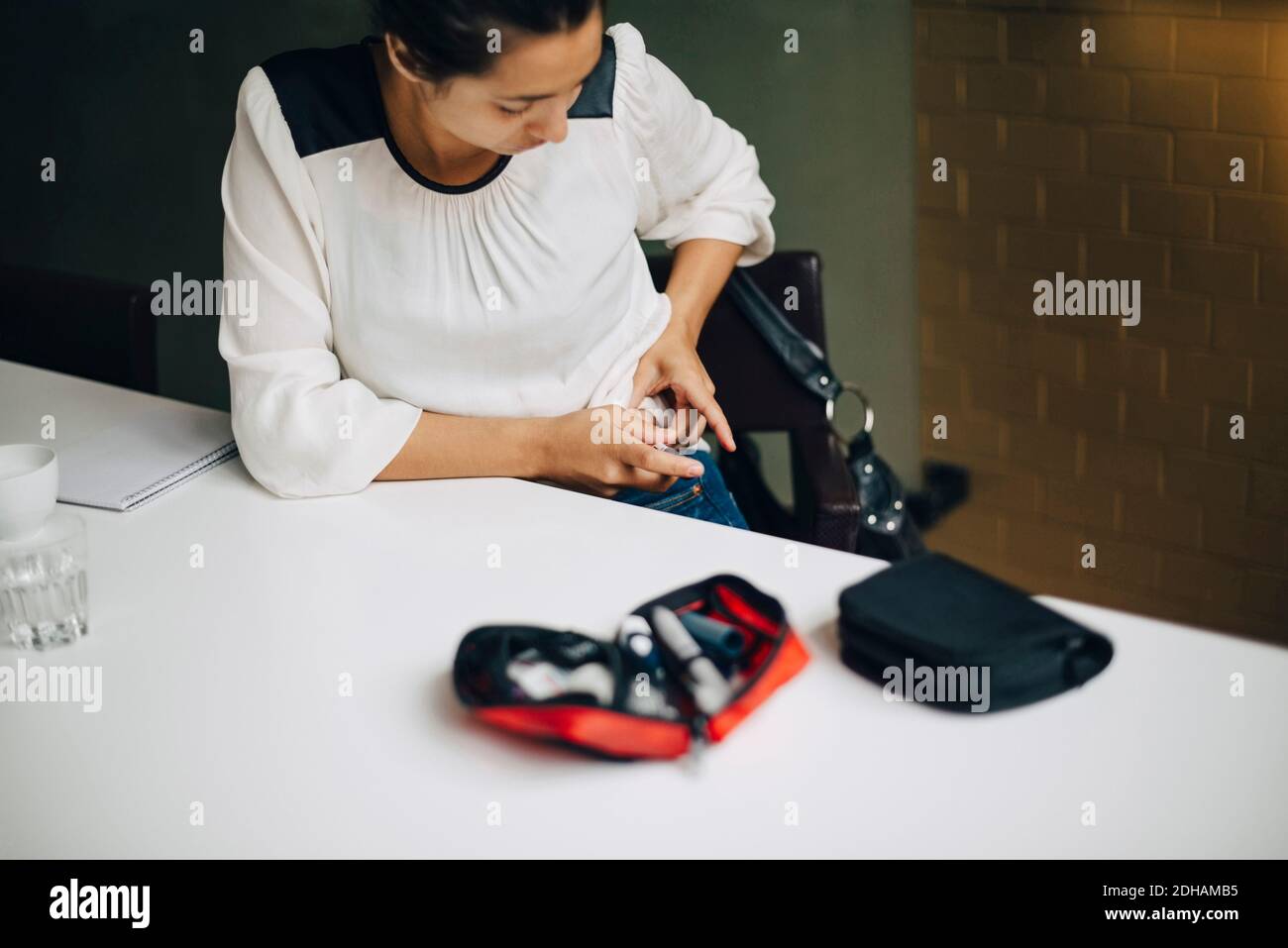 Mujer de negocios inyectando insulina en el abdomen mientras se sienta en la mesa Foto de stock
