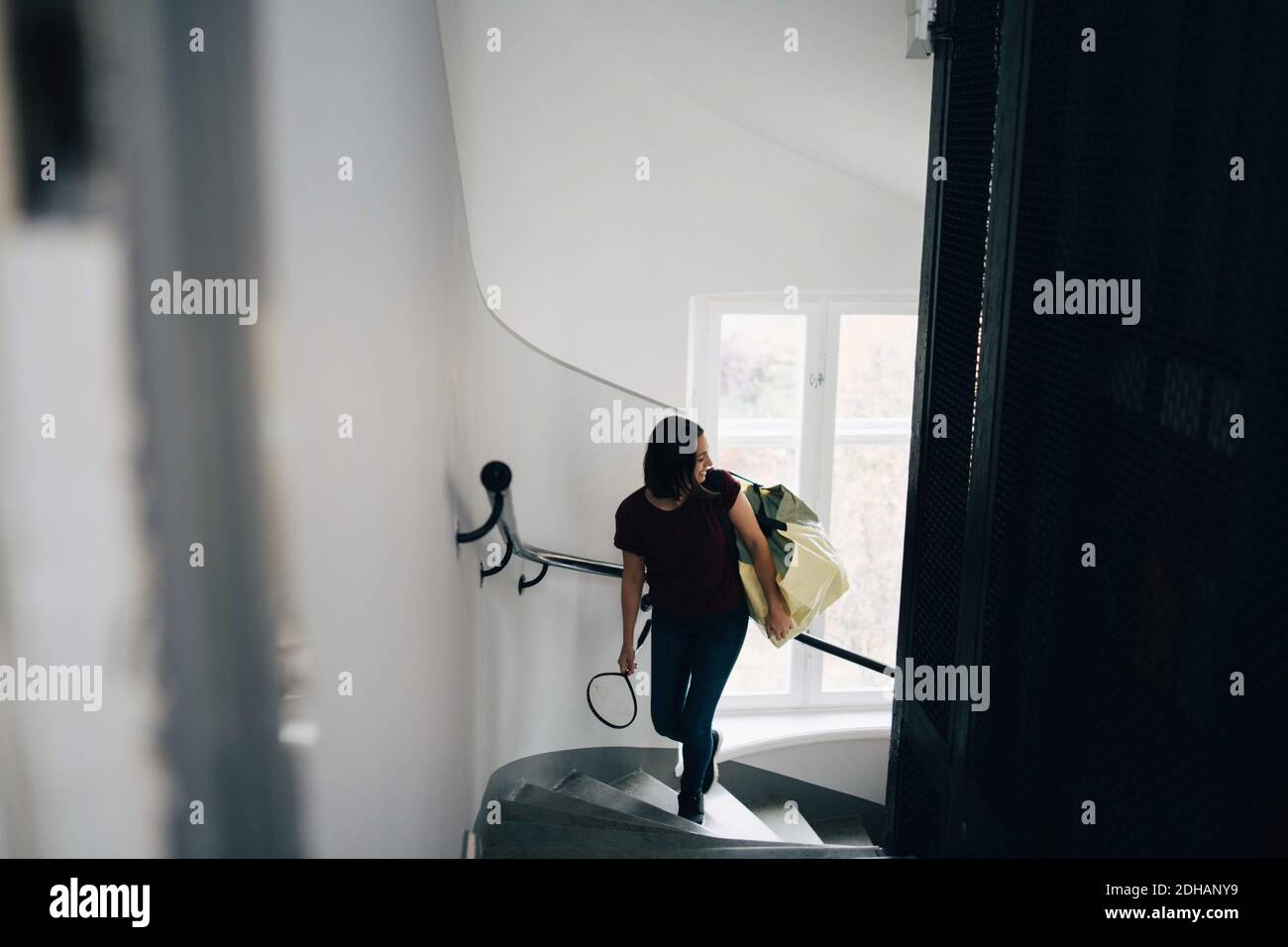 Vista de gran ángulo de la mujer que lleva la bolsa y la raqueta de bádminton mientras escalan escalones en casa nueva Foto de stock