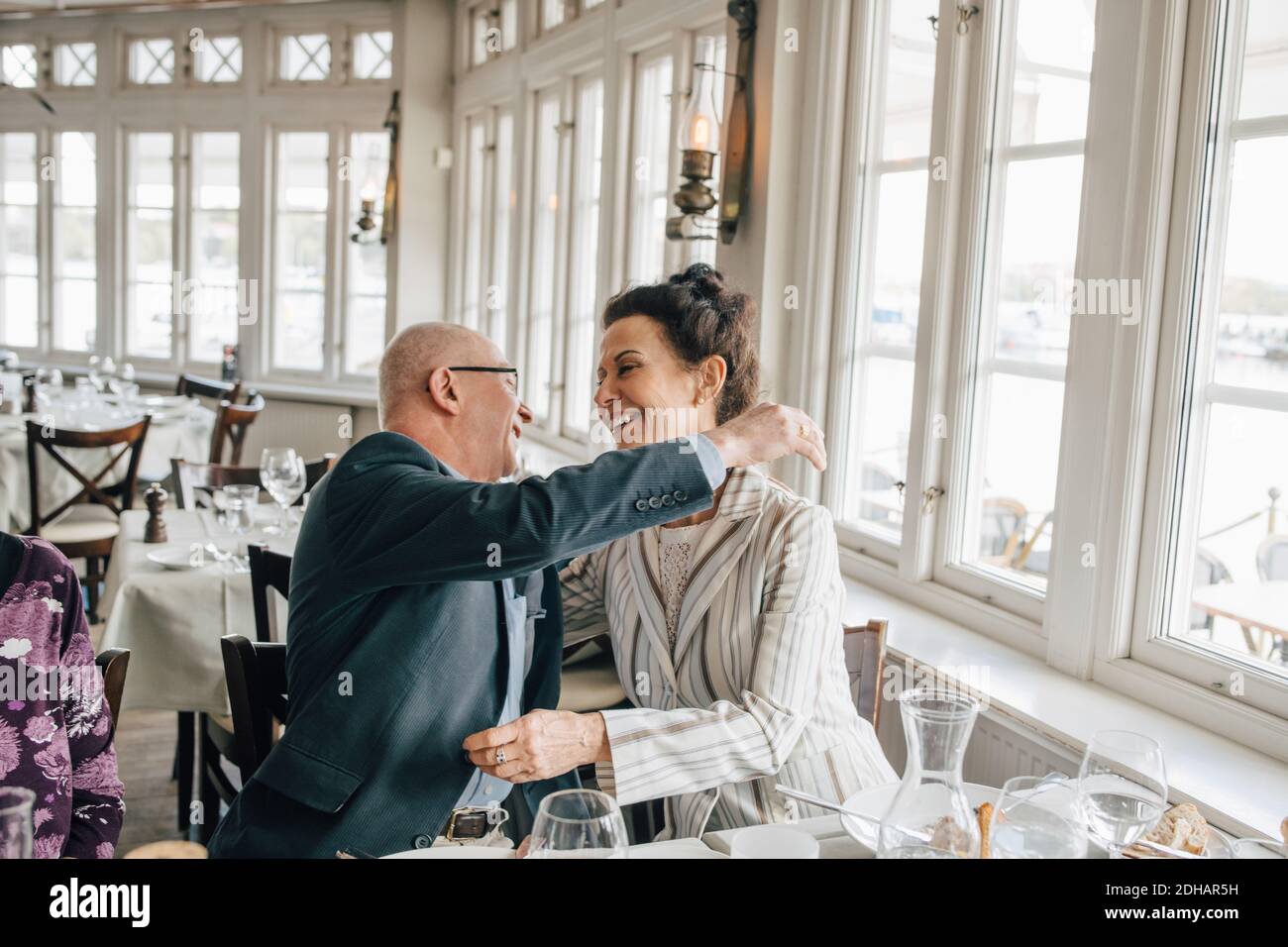 Hombre mayor abrazando a la mujer mientras estaba sentado en el restaurante Foto de stock
