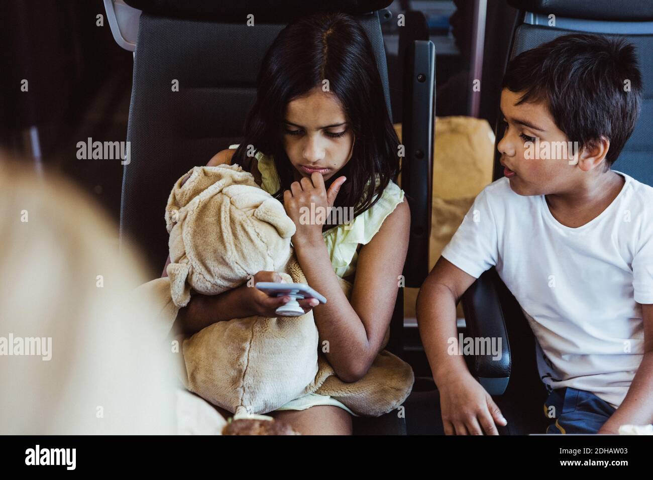 Chico mirando a la hermana usando el teléfono inteligente mientras viajas tren Foto de stock
