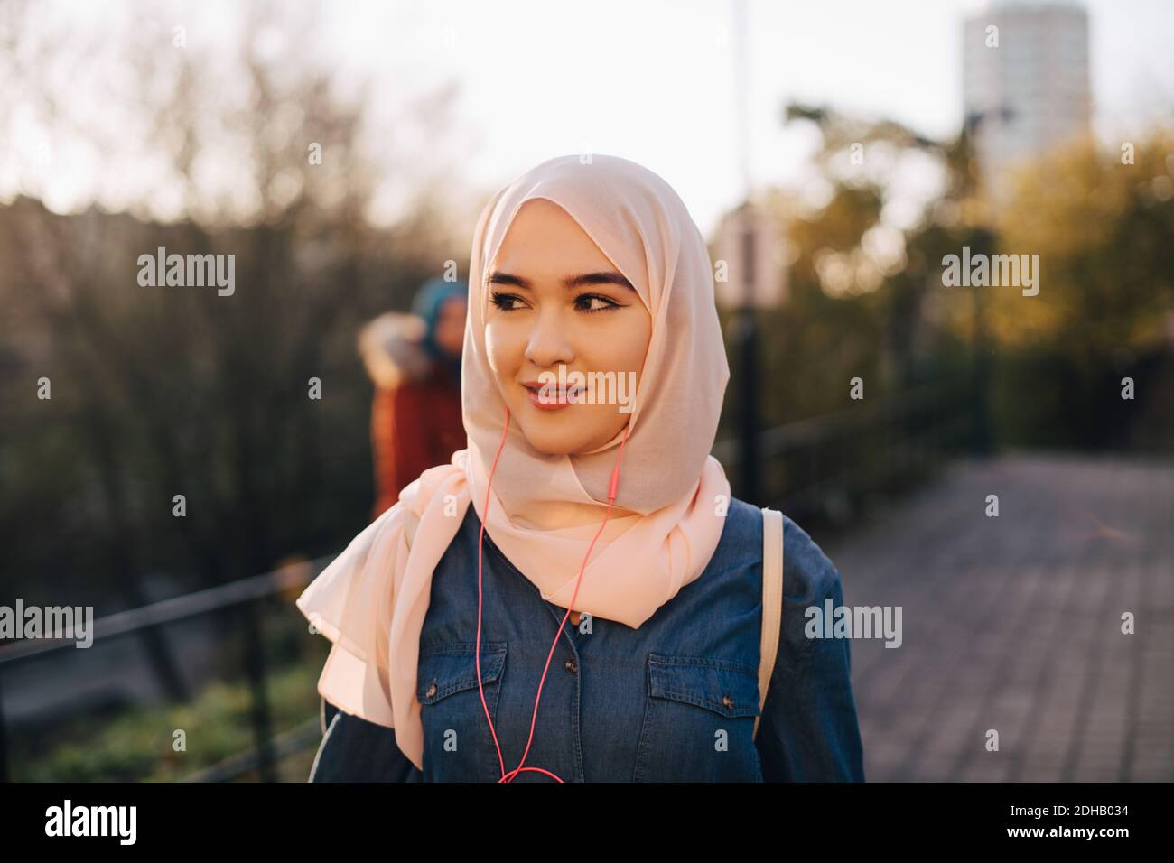 Una joven musulmana segura escuchando música mirando hacia fuera contra la claridad cielo Foto de stock