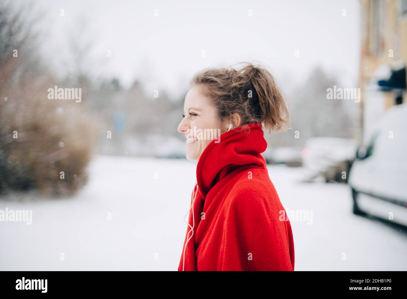 Vista lateral de una joven sonriente en el suéter rojo de pie en el campo nevado Foto de stock