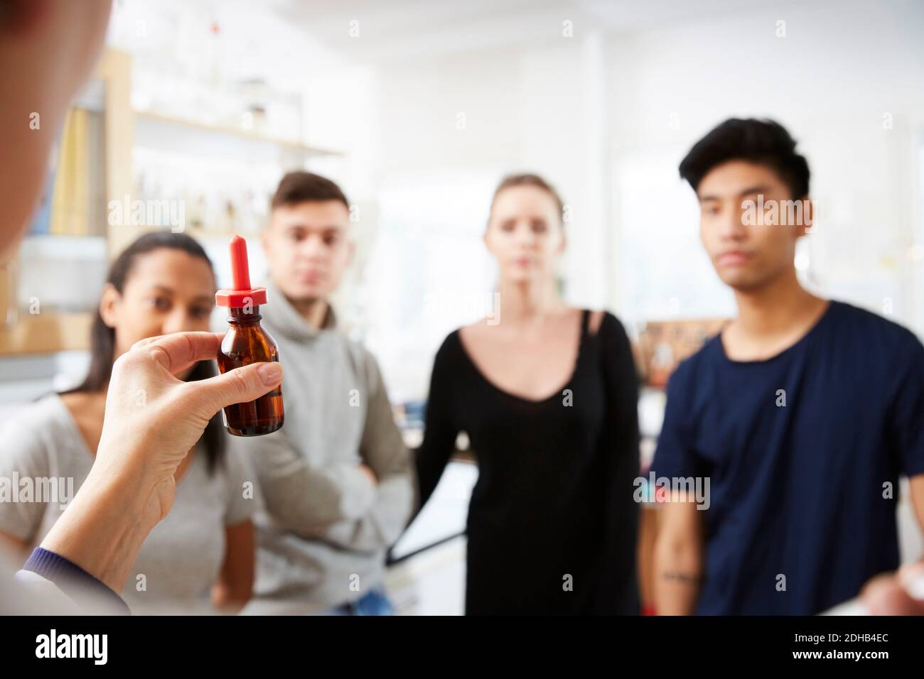 Imagen recortada de maestra madura mostrando solución mientras explicaba a jóvenes estudiantes multiétnicos en laboratorio Foto de stock