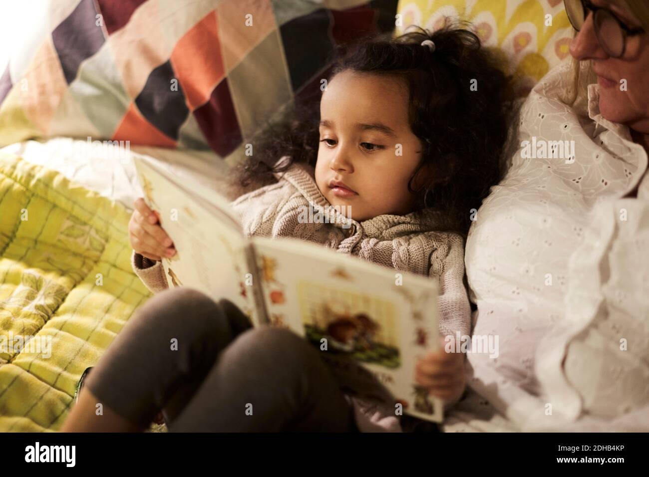 Vista en ángulo alto de la abuela leyendo libro a la nieta cama en casa Foto de stock