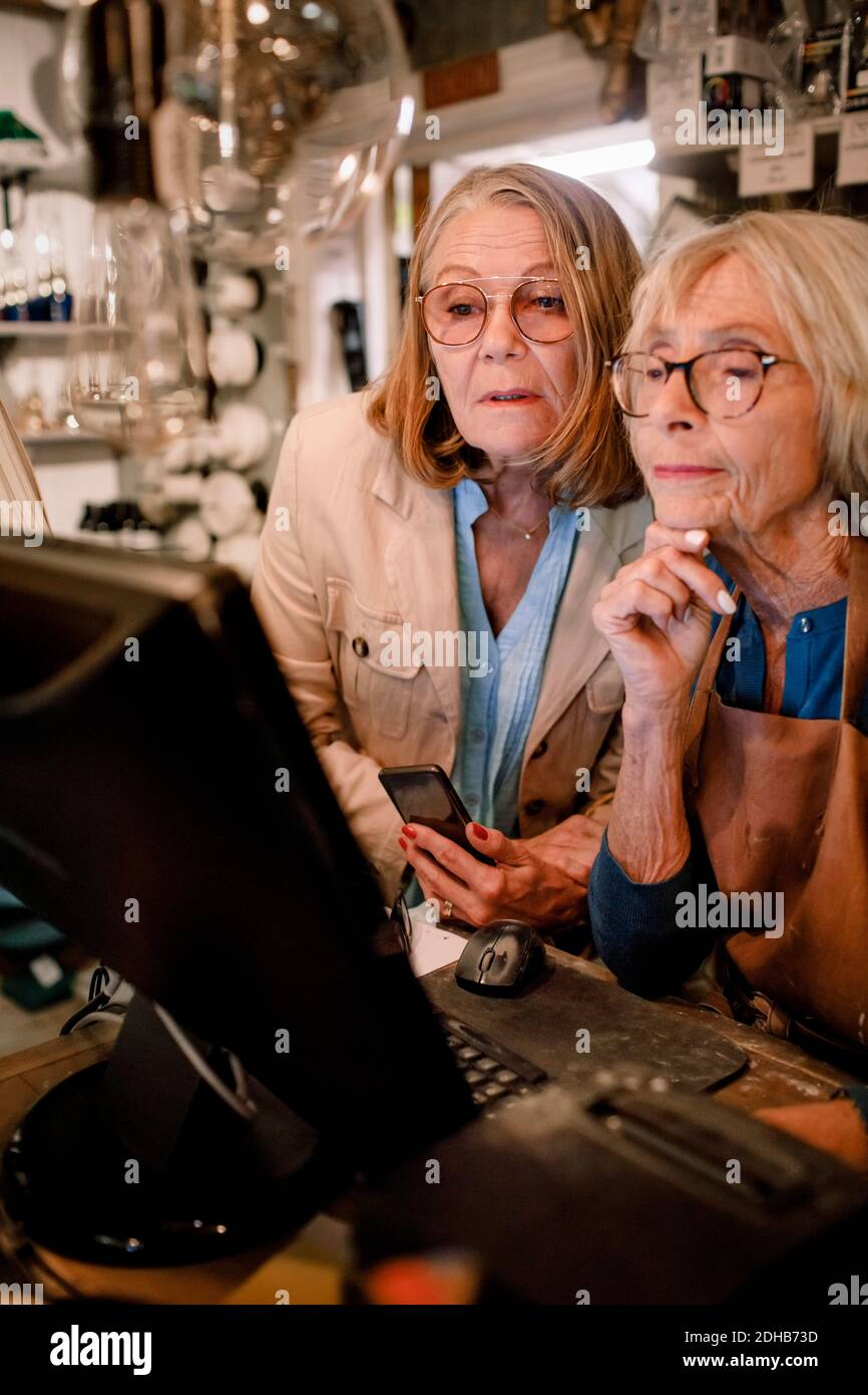 Una mujer mayor cliente y una vendedora mirando el monitor de la computadora almacén de hardware Foto de stock