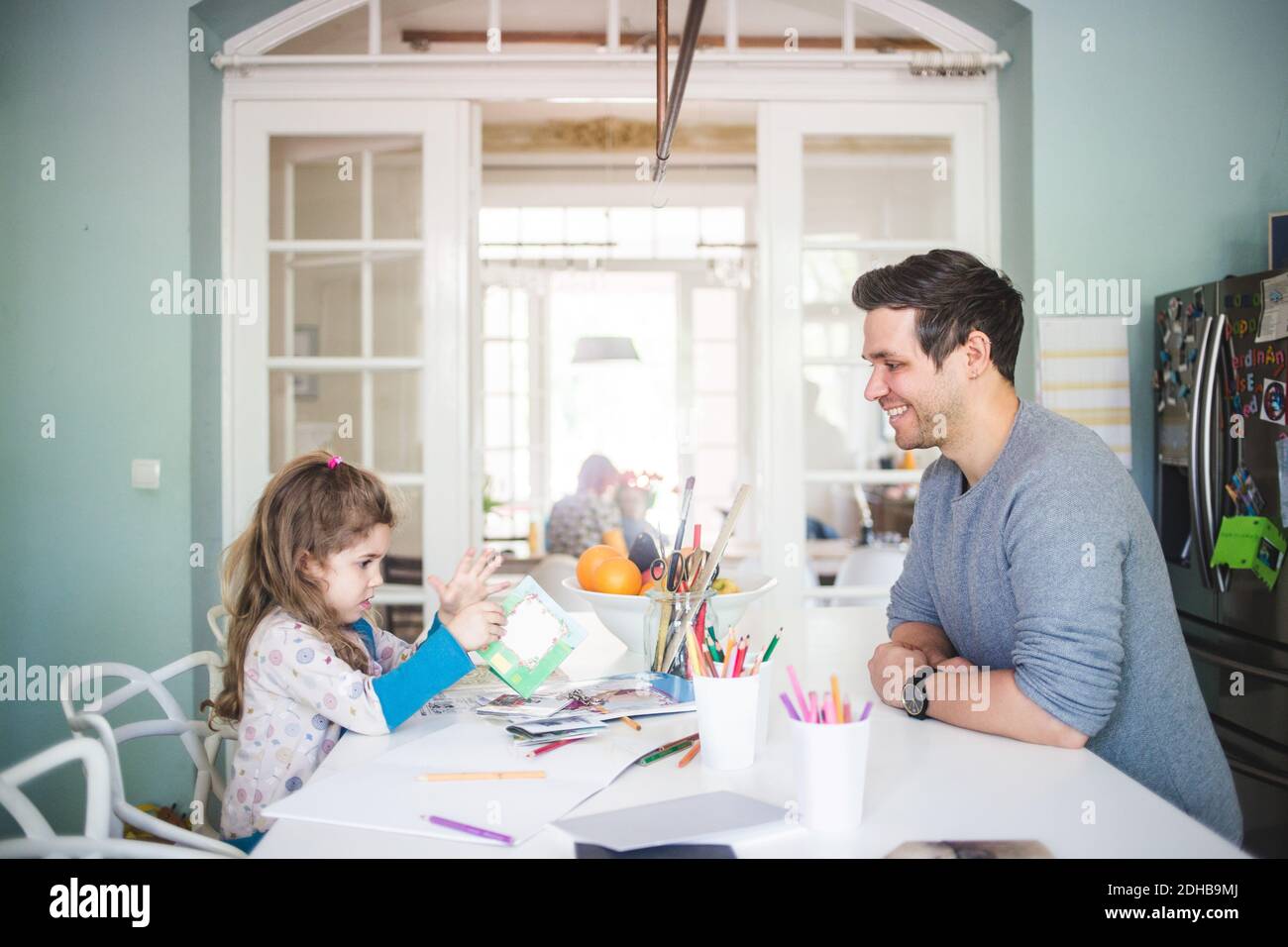 Padre sonriente mirando a la chica sosteniendo un libro de fotos en la cocina Foto de stock