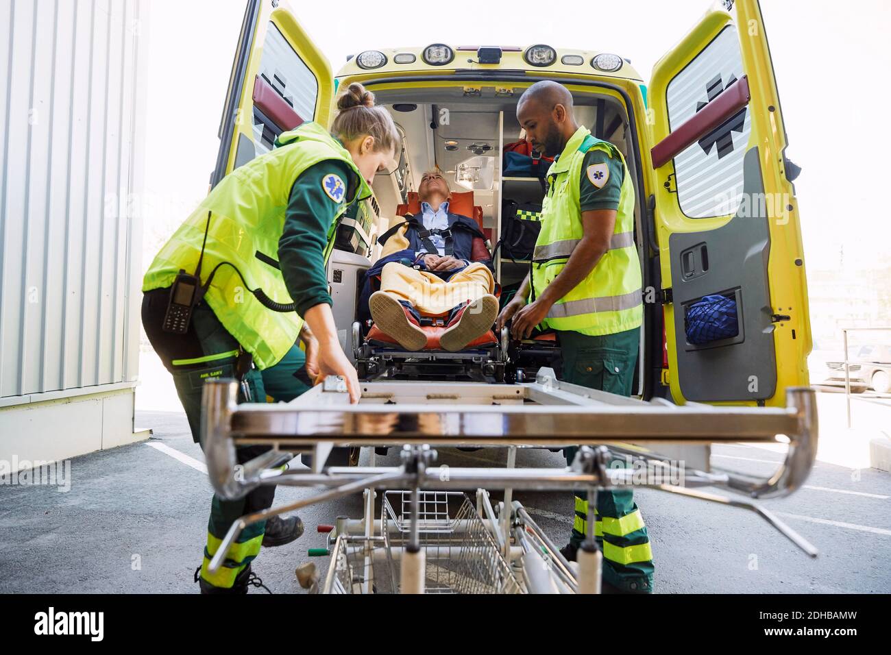 Trabajadores de la salud que sacan a un paciente maduro de una ambulancia en una camilla del hospital Foto de stock