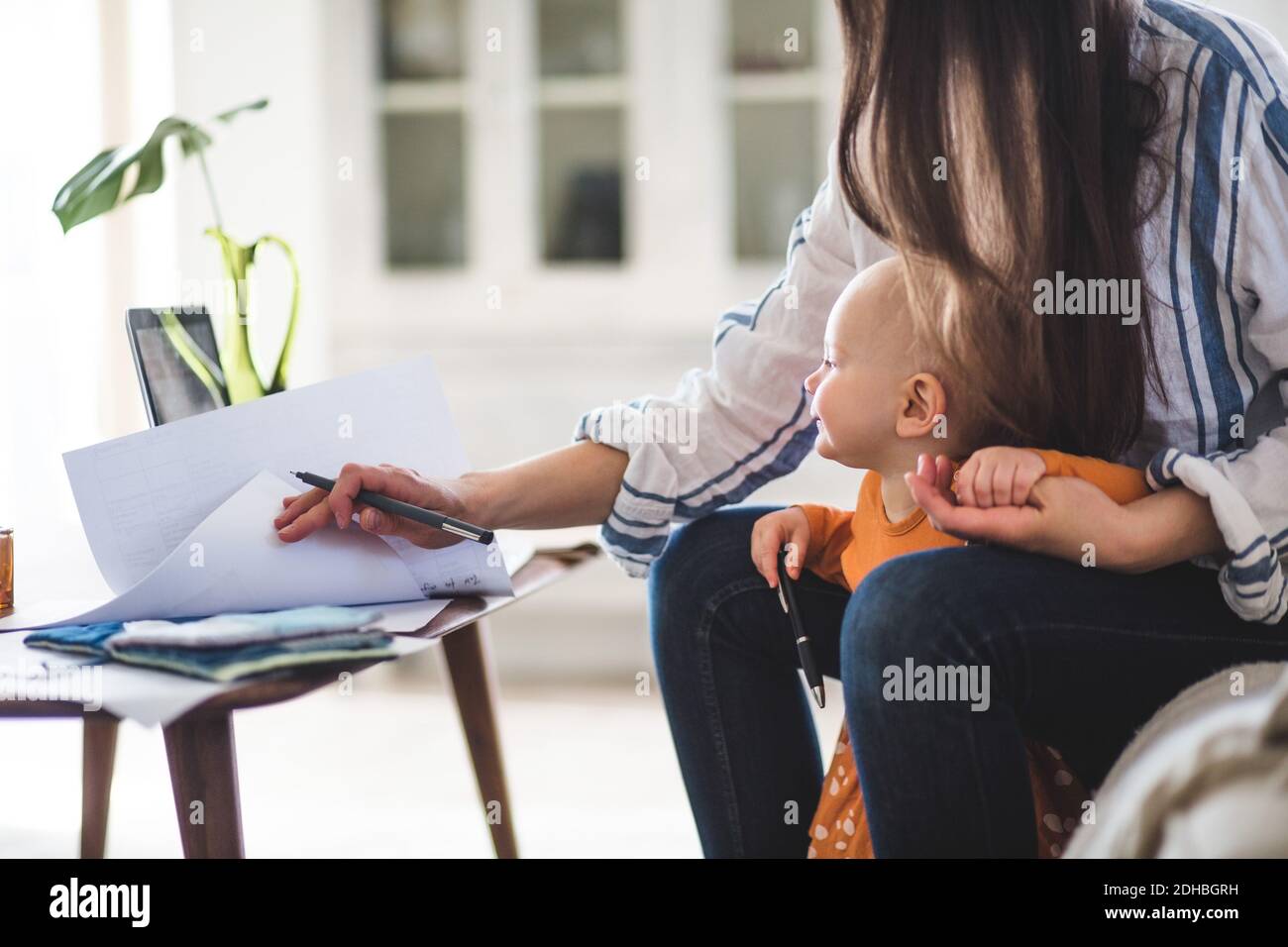 Sección intermedia de la madre trabajadora examinando documentos con la niña en oficina en casa Foto de stock