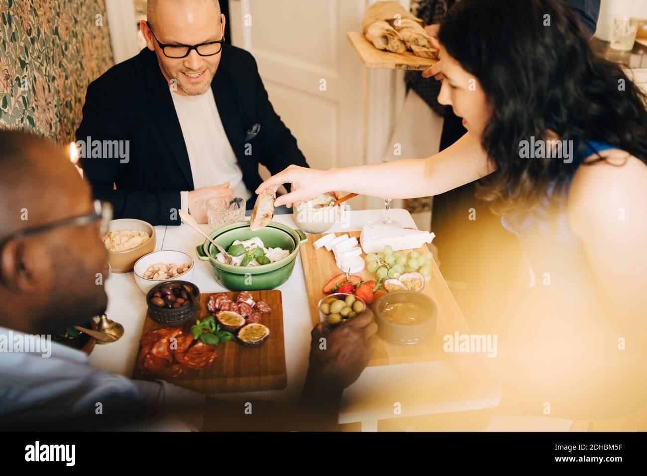 Mujer sentada con amigos masculinos mientras cena durante la fiesta en casa Foto de stock