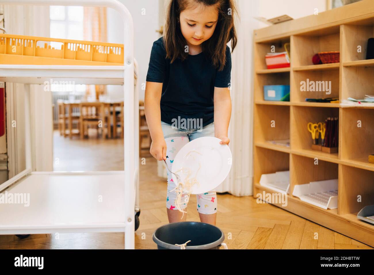 Chica que lanza espaguetis en la basura puede en el jardín de infantes Foto de stock