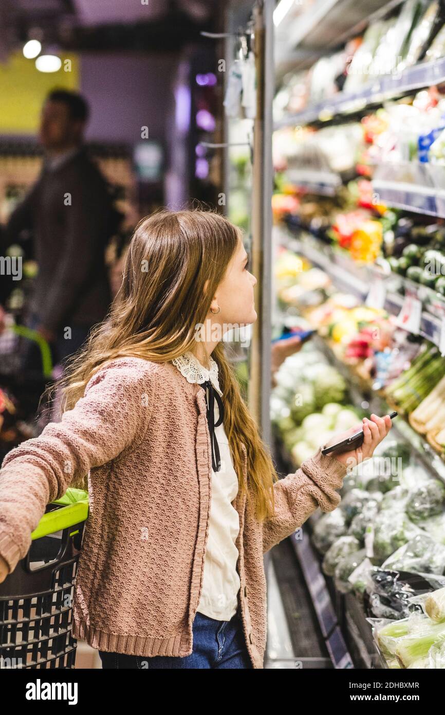 Vista lateral de la chica mirando verduras en los estantes almacenar Foto de stock
