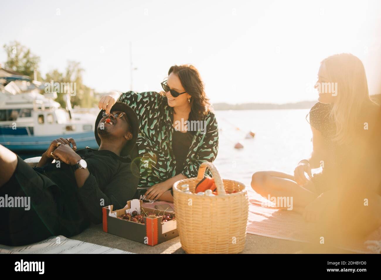 Amigos disfrutando de las cerezas mientras se sentaba en el embarcadero contra el lago en verano Foto de stock
