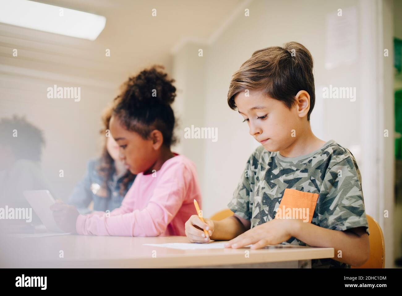 Niño sentado con un amigo escribiendo sobre el papel en el escritorio aula Foto de stock