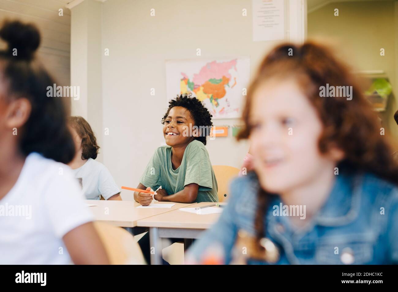 Sonriente chico sentado con amigos en el escritorio en el aula Foto de stock