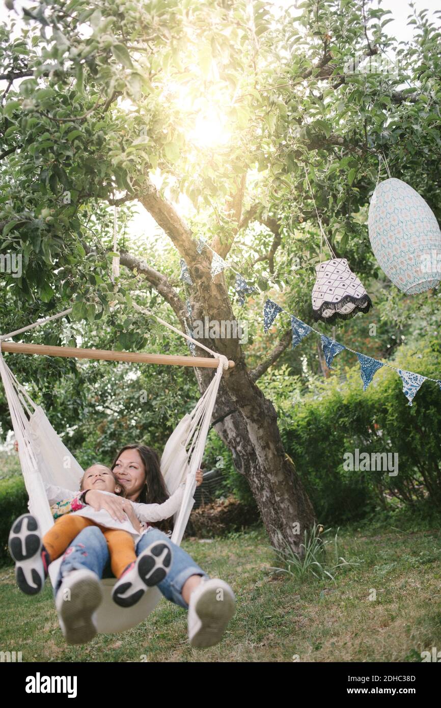 Madre e hija sonriendo mientras se balanceaba en una hamaca en el patio trasero Foto de stock