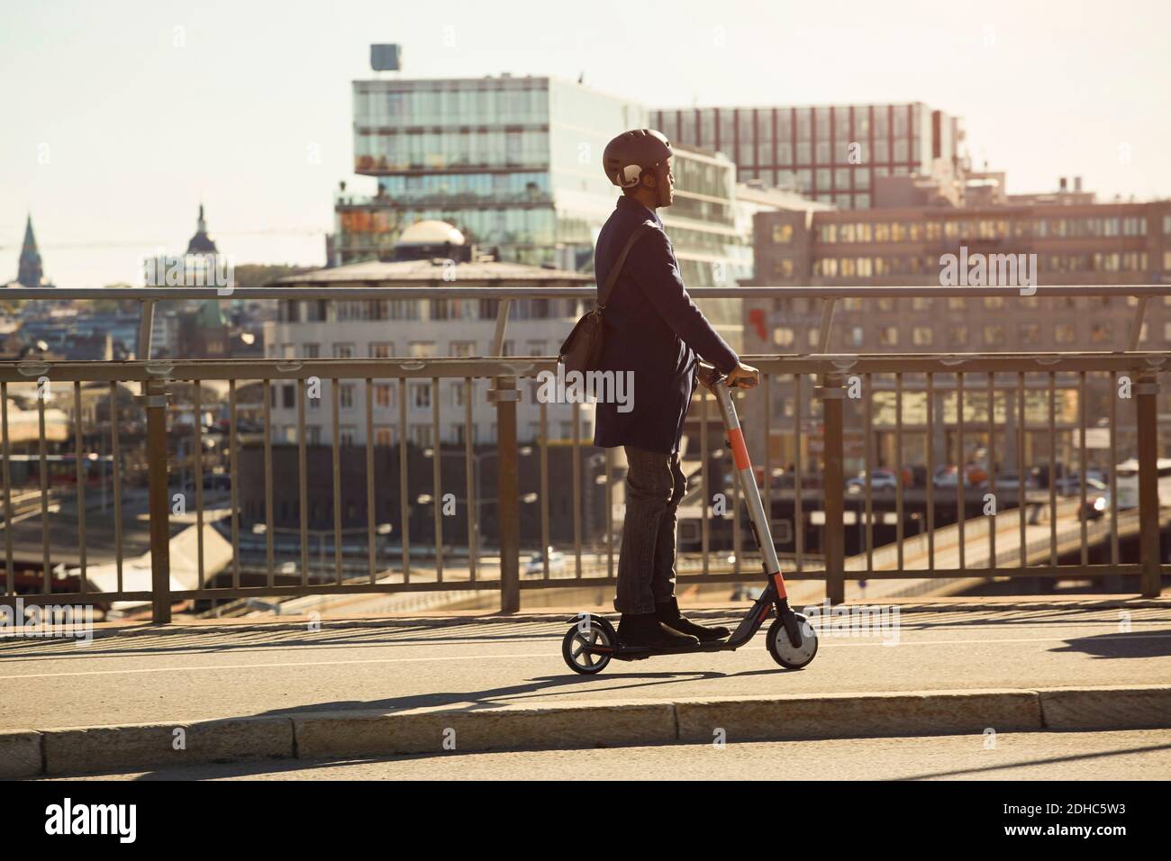 Toda la longitud de hombre joven montando scooter eléctrico de empuje puente en la ciudad Foto de stock
