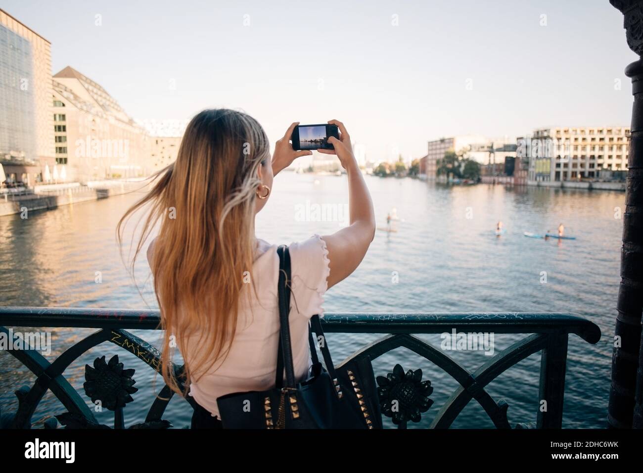 Vista trasera de la joven fotografiando el río a través del teléfono móvil en la ciudad Foto de stock