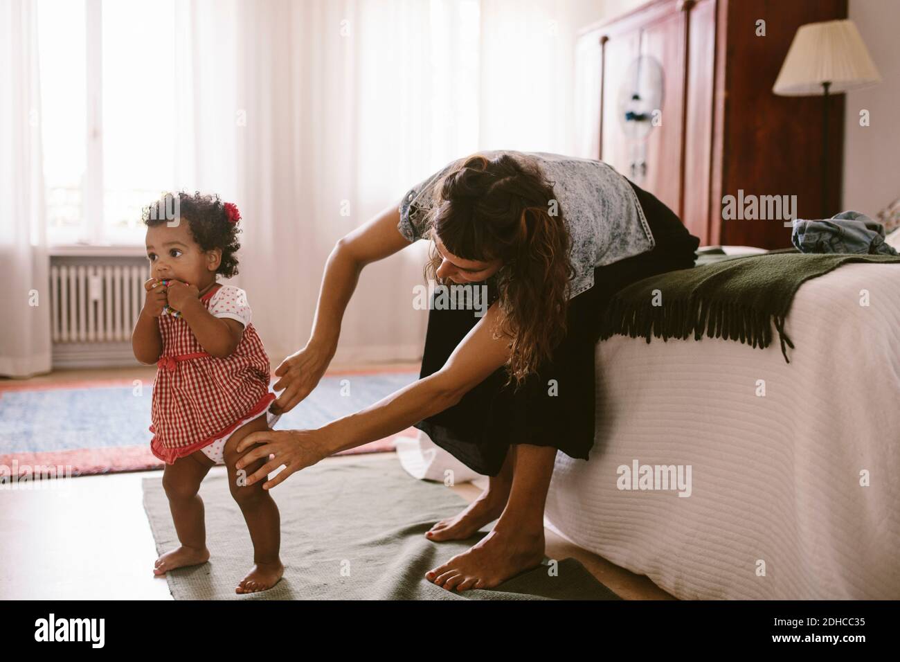 Mujer adulta mediana ajustando el pañal de su hija mientras está sentada cama en casa Foto de stock
